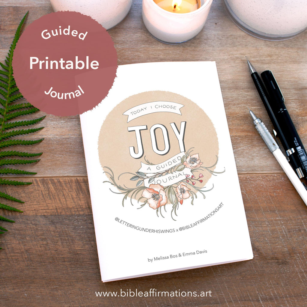 Printed Joy Journal booklet on wooden desk arranged with fern leaf, candles & pencils